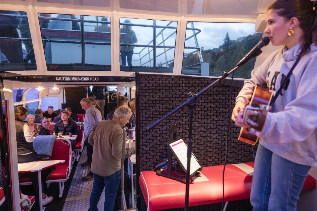 BrookedV_MDC_May25-7-min Female musician performing with acoustic guitar and microphone on a cruise.